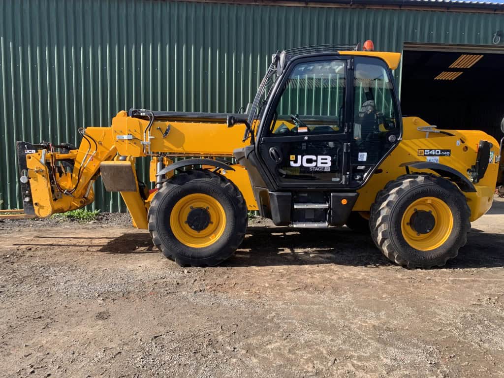 Yellow JCB telehandler parked outside green warehouse